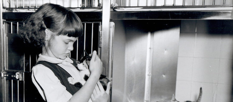Young girl with kitten standing next to cage