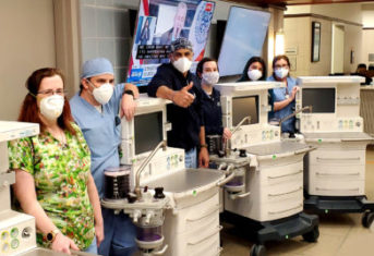 A team of veterinarians wearing masks stands around four ventilators