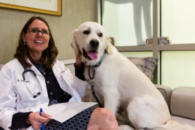 A veterinarian sits on a couch with a dog