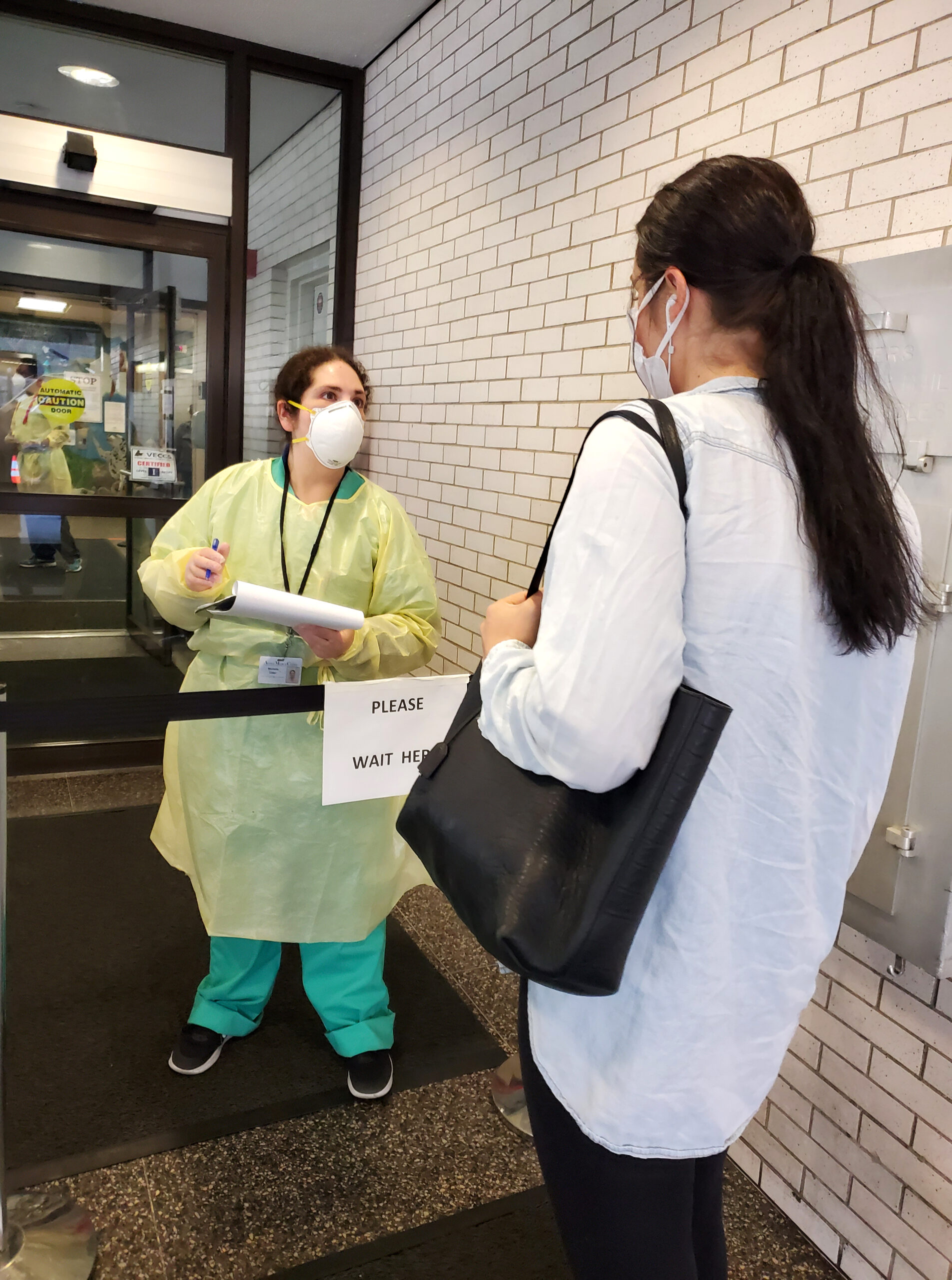 A masked veterinary professional assists a client at the front door of the Animal Medical Center of New York City